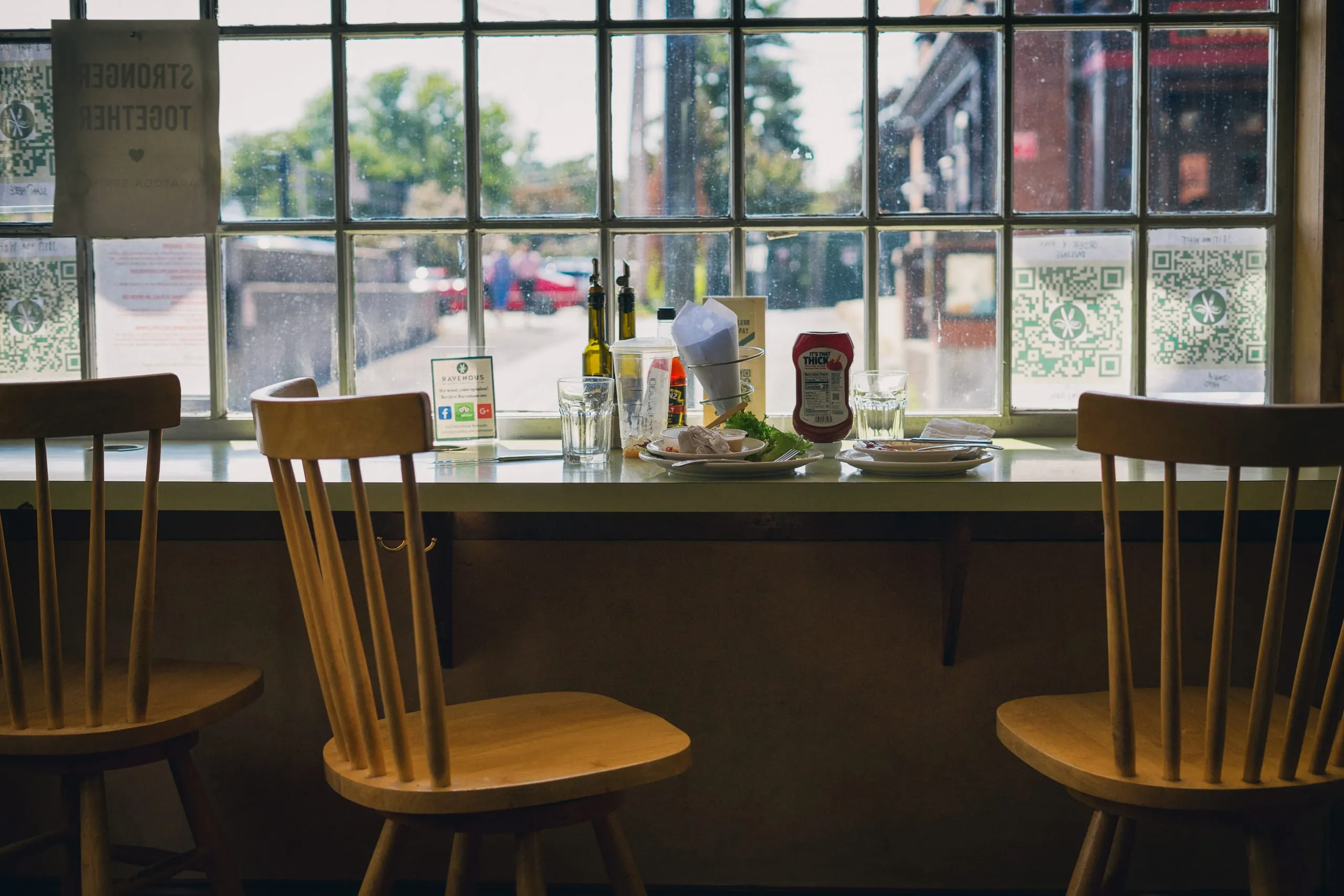 Empty wooden chairs face a diner window ledge cluttered with condiments and dishes in Saratoga Springs.