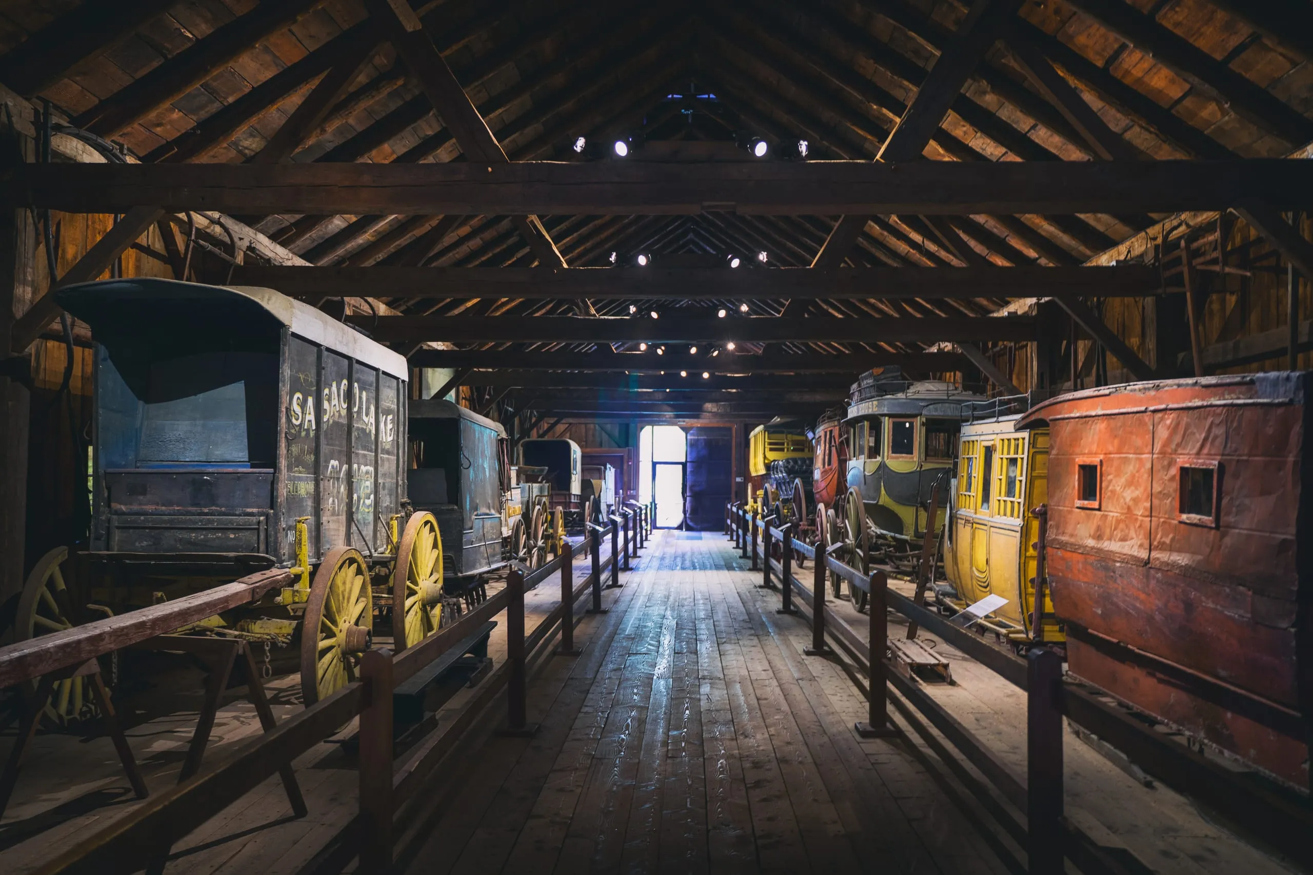 Rows of antique horse-drawn coaches and wagons lined up inside a timber-framed barn in Vermont.