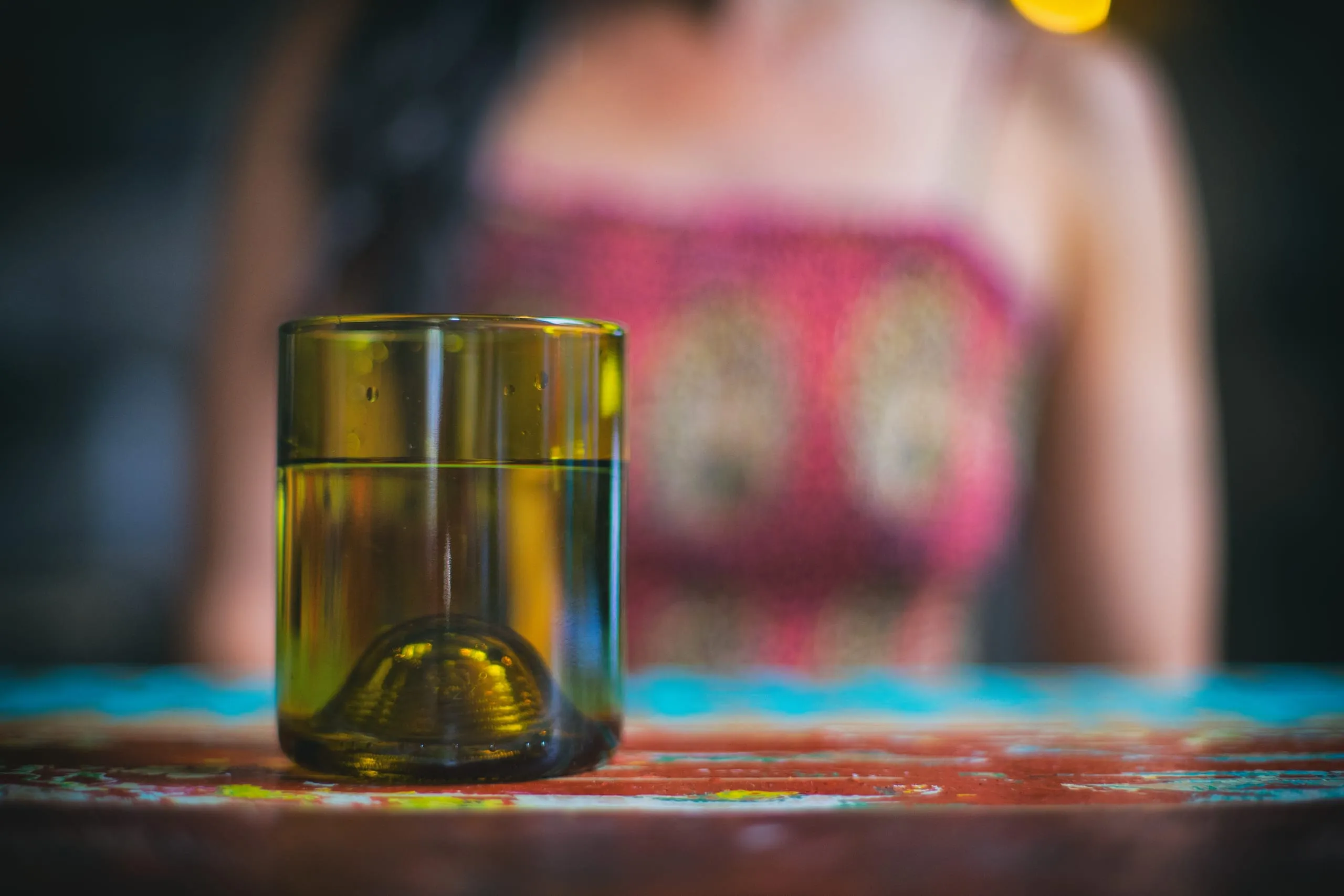 Moody bar detail with a glass in warm light and a figure in a sequined top beyond, Pittsburgh