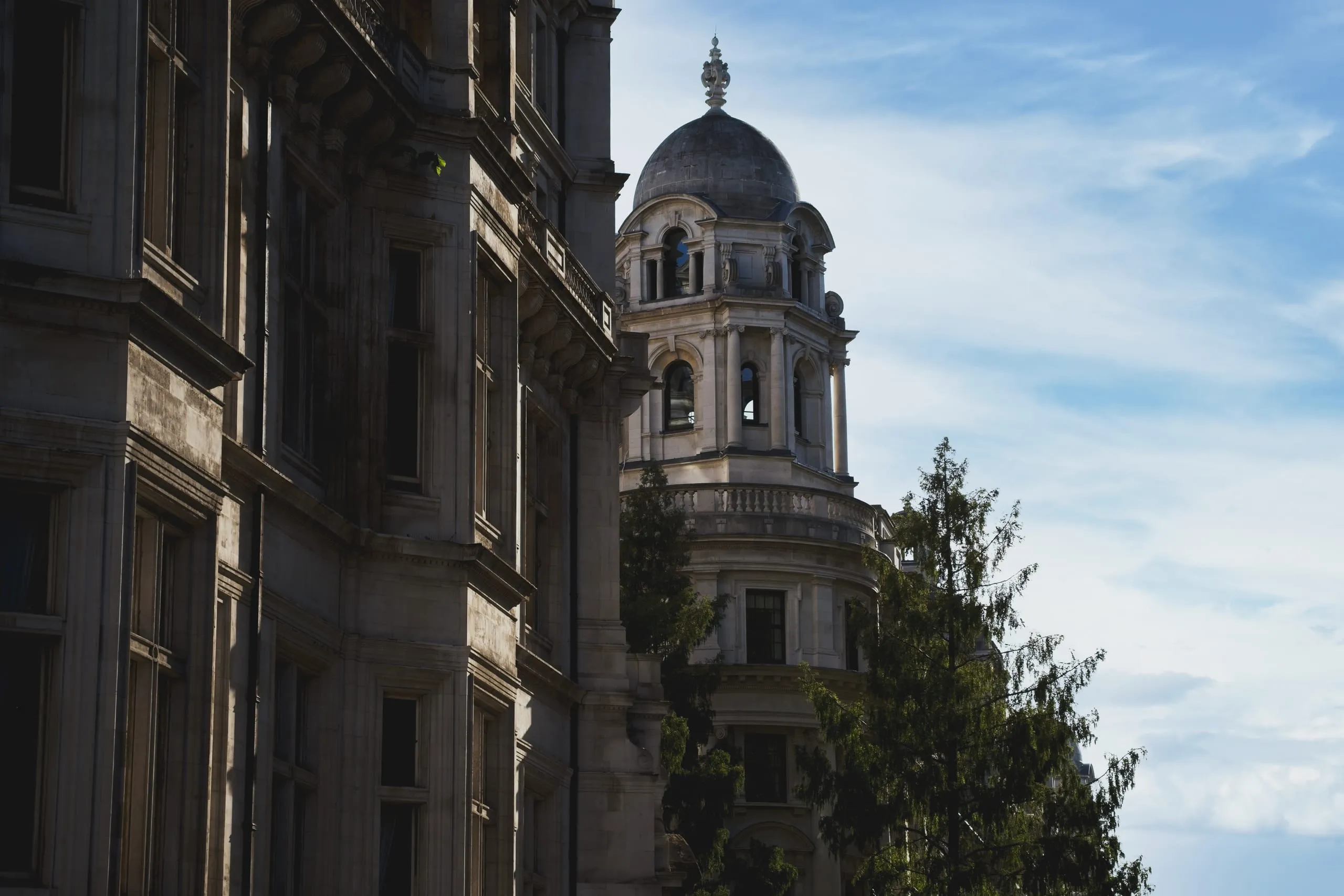 A photograph of an ornate domed corner tower on a Victorian government building rising above rooftops and trees near Westminster, London.