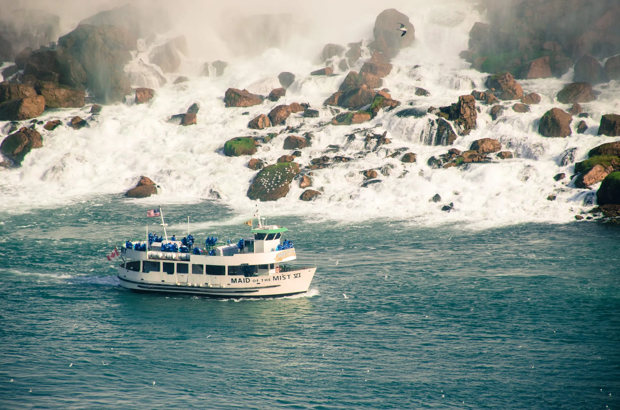 The Maid of the Mist VI tour boat, packed with blue-poncho riders, motors past rapids below Niagara Falls.