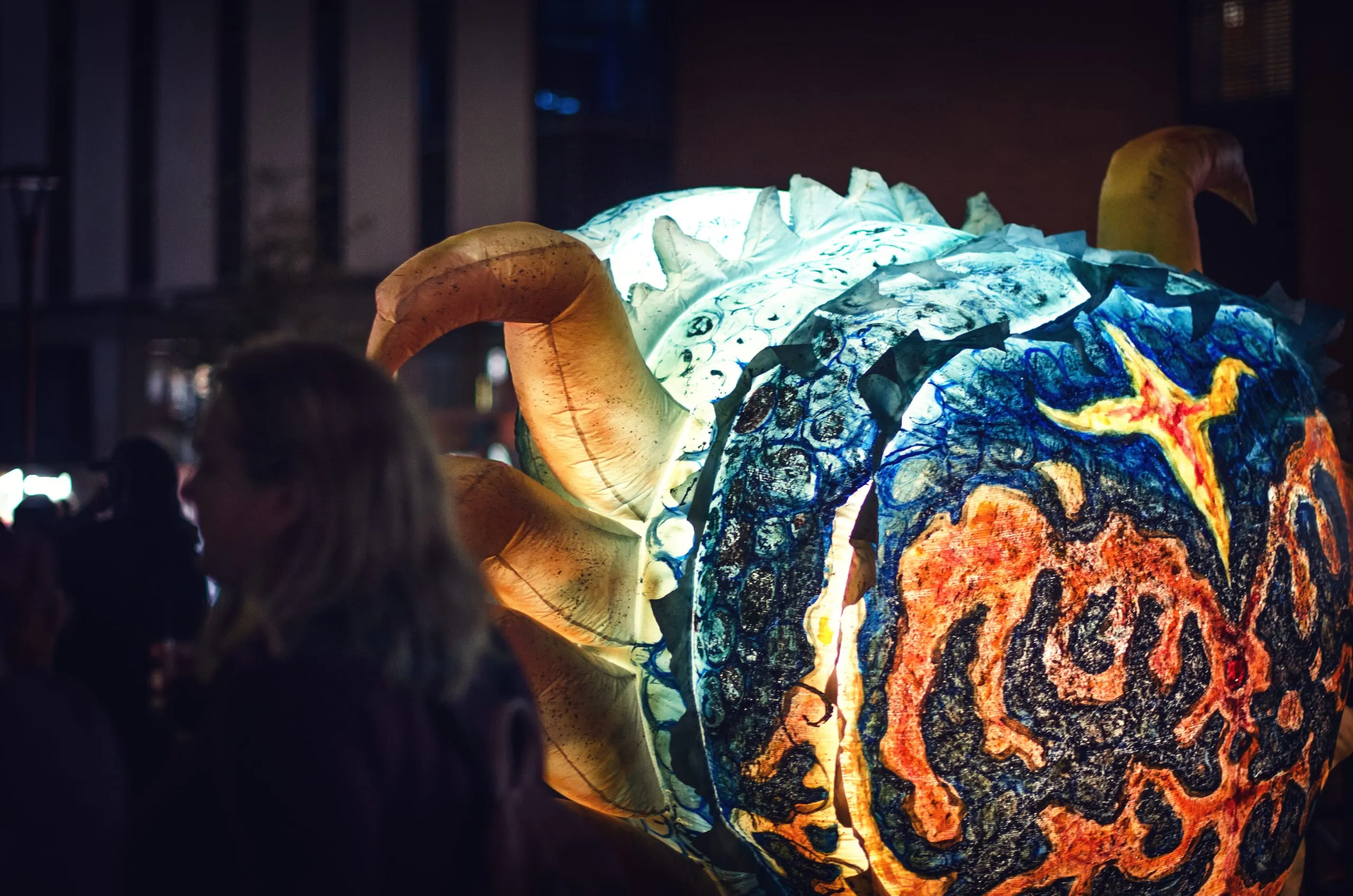 Glowing blue-and-orange lantern creature carried through a crowd at night, Rochester
