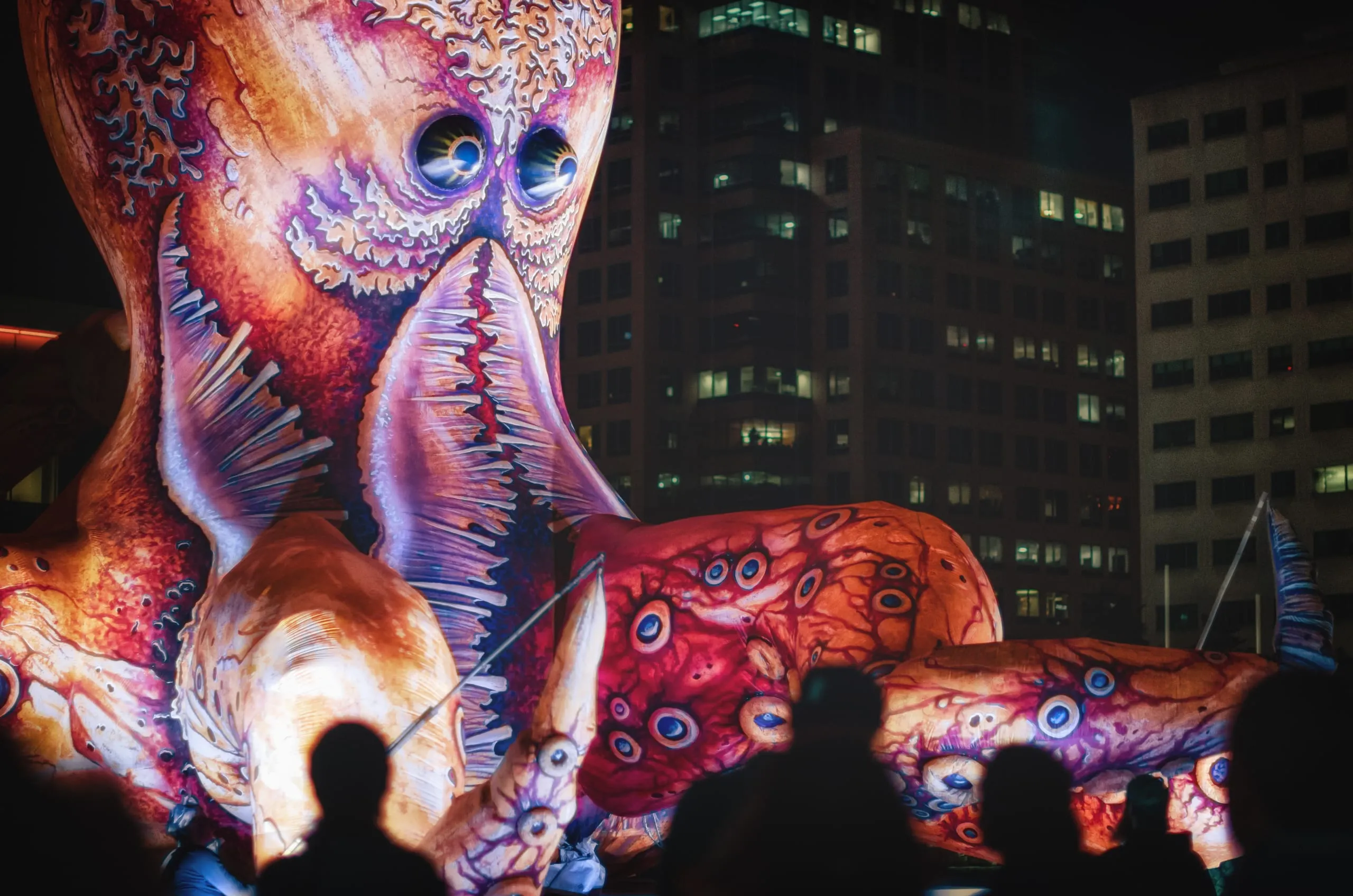 Giant illuminated octopus puppet glowing against downtown Rochester towers at night