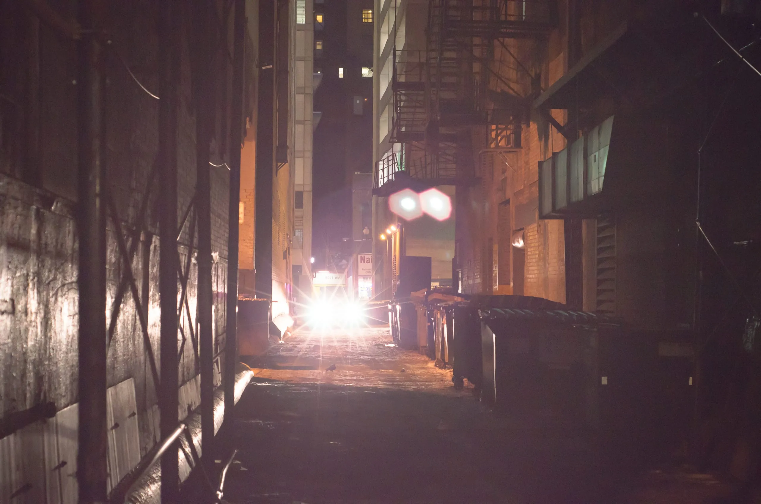 Chicago night alley washed in purple with headlight glow approaching