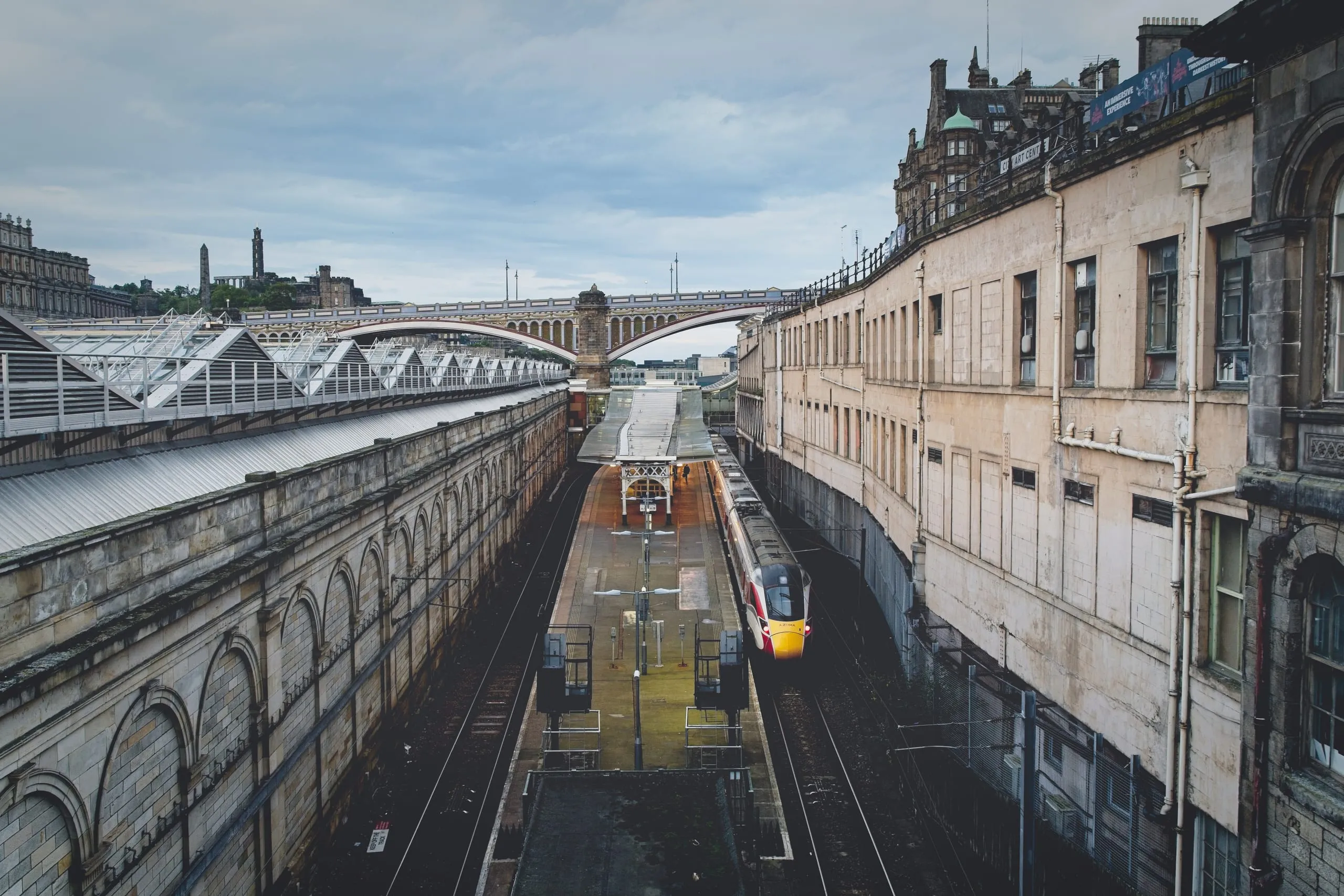 A color photograph of a train at Edinburgh Waverley railway station, with the North Bridge and Calton Hill's Nelson Monument visible in the distance.