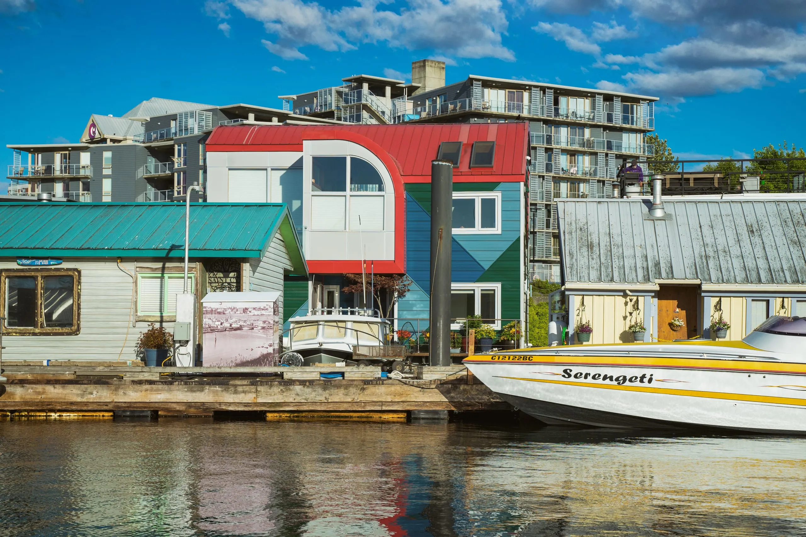 Red and teal houseboats with a small runabout moored in Victoria's harbor