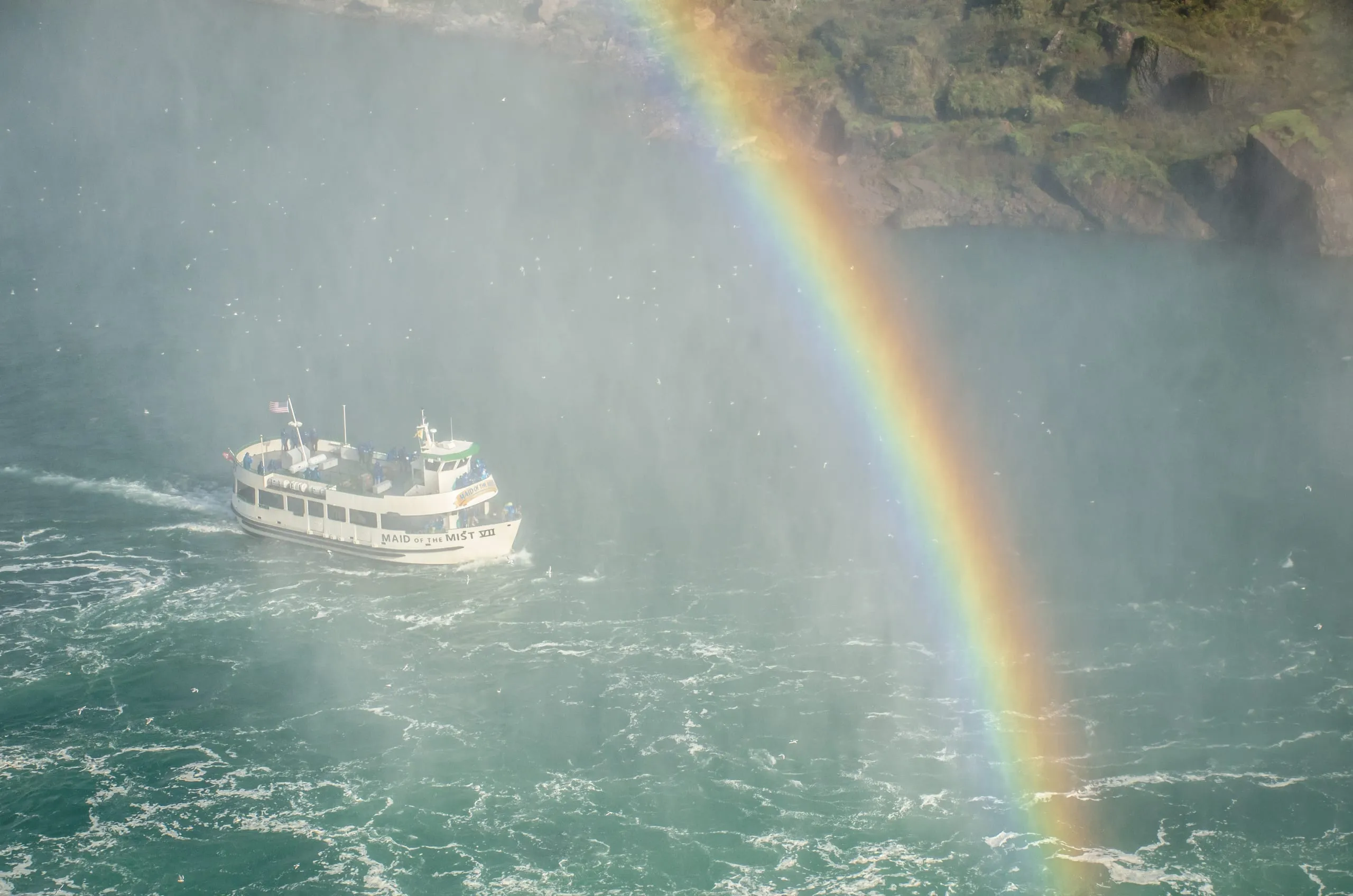 Tour boat passing beneath a rainbow arcing through Niagara's mist