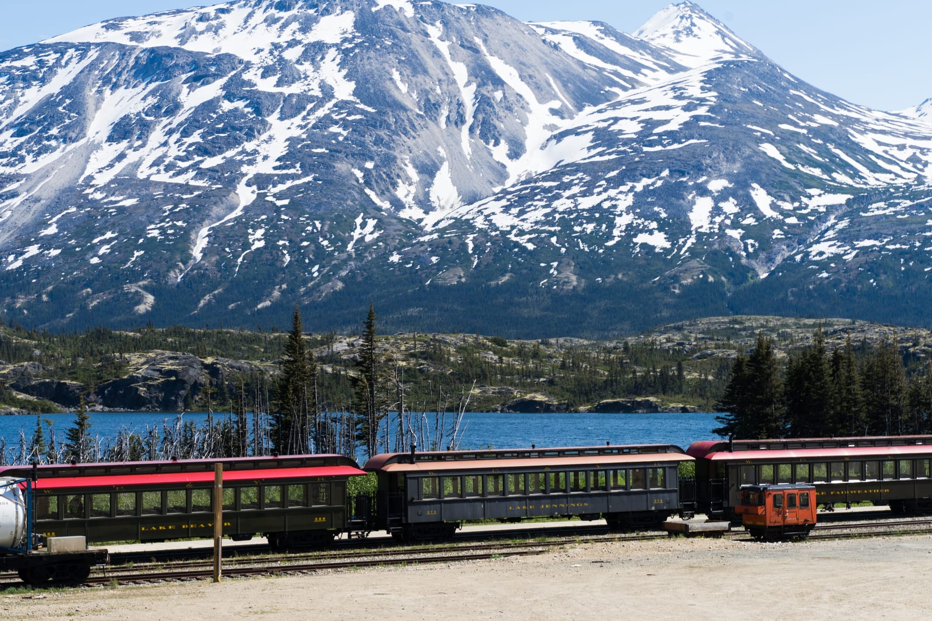 White Pass and Yukon Route train winding past a snowy peak and turquoise alpine lake